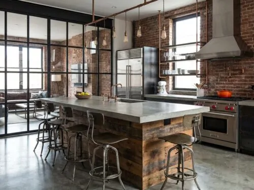 Cocina con mampara de cristal con marco de metal negro e isla central blanca en un espacio diáfano