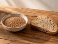 Grains de petit épeautre crus et tranche de pain au levain sur table en bois