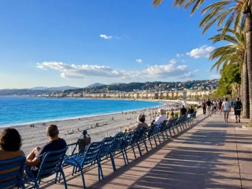 Promenade en bord de mer typique de la Côte d'Azur avec chaises bleues et palmiers