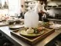 Cloche en verre remplie de fumée blanche posée sur une assiette de burrata dans une cuisine de restaurant